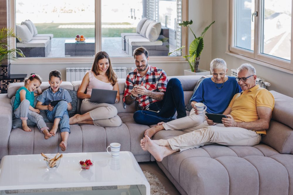Happy extended family relaxing on the sofa at home and using connected technology.