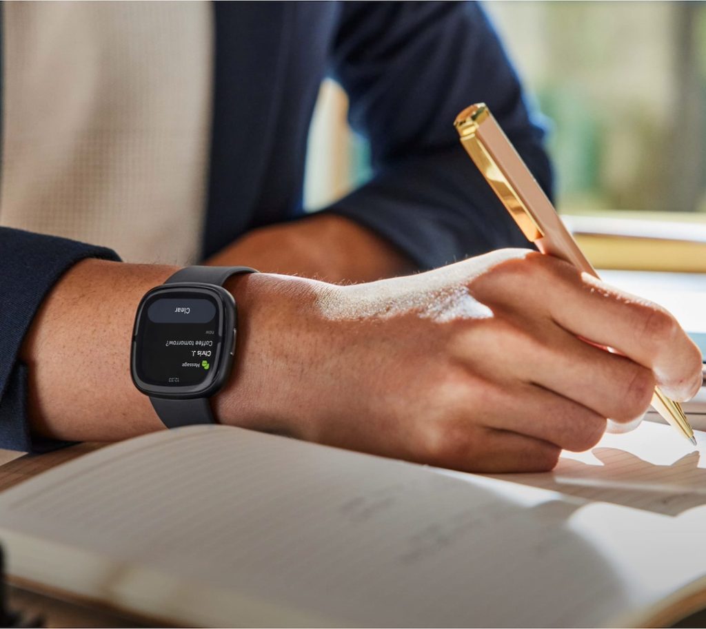 A man wearing the Fitbit wearable tech device while writing in a notebook.